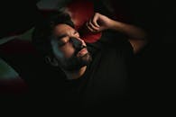 A bearded man lies in a dimly lit room, peacefully resting with closed eyes.